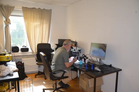 En man arbetar vid ett skrivbord i ett ljust rum med dator och stolar.